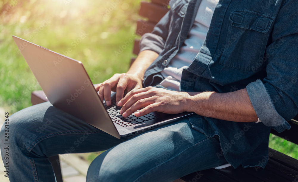 Naklejka premium Close up view of multicultural businessman siting on a bench and working with his laptop