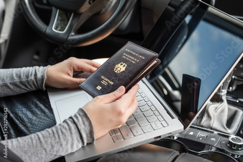 Woman in the car with laptop and germany passport. Business concept. © flowertiare