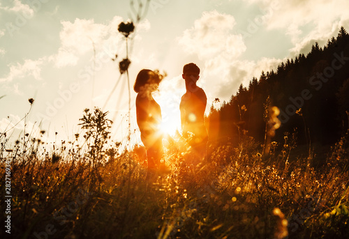 In love couple silhouets among high grass on sunset meadow photo