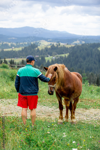 man near horse in field mountains on background
