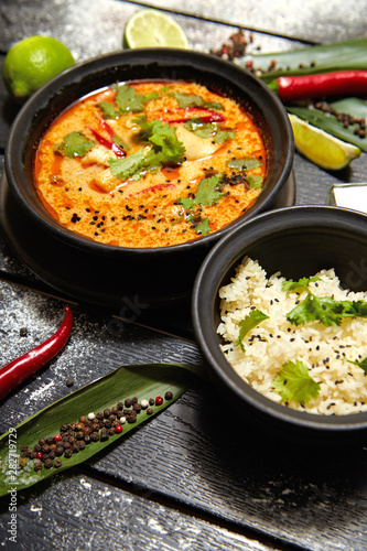 Asian dish on a black plate. Tom yum with rice