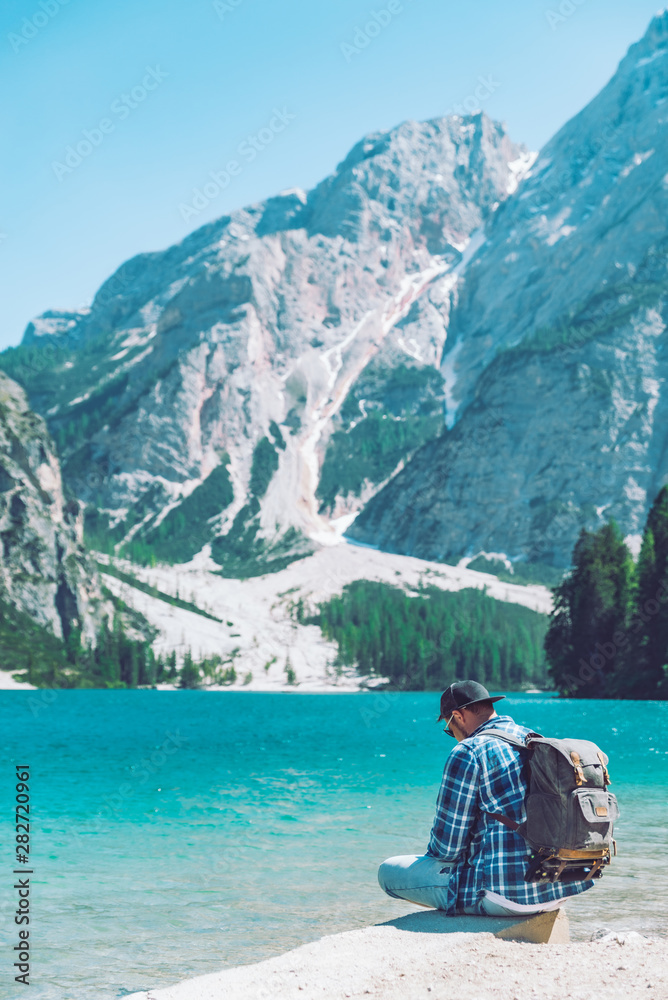 Fototapeta premium man sitting on the beach of the lake with backpack mountains in background