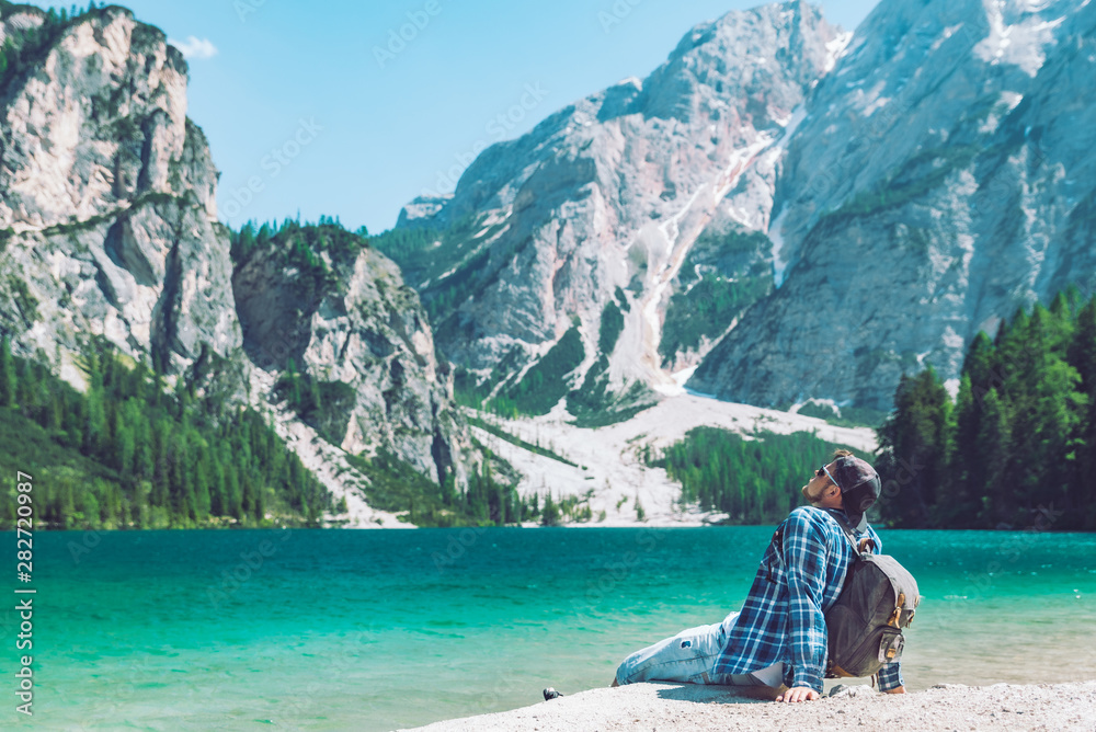 man sitting on the beach of the lake with backpack mountains in background man sitting on the beach of the lake with backpack mountains in background