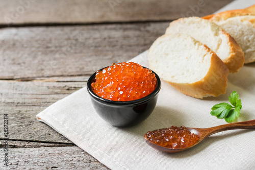 Red caviar in black bowl on wooden background
