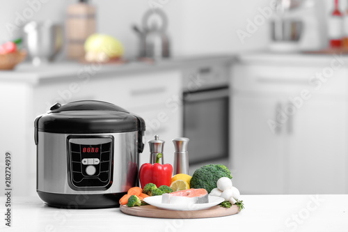 Modern multi cooker and products on table in kitchen. Space for text