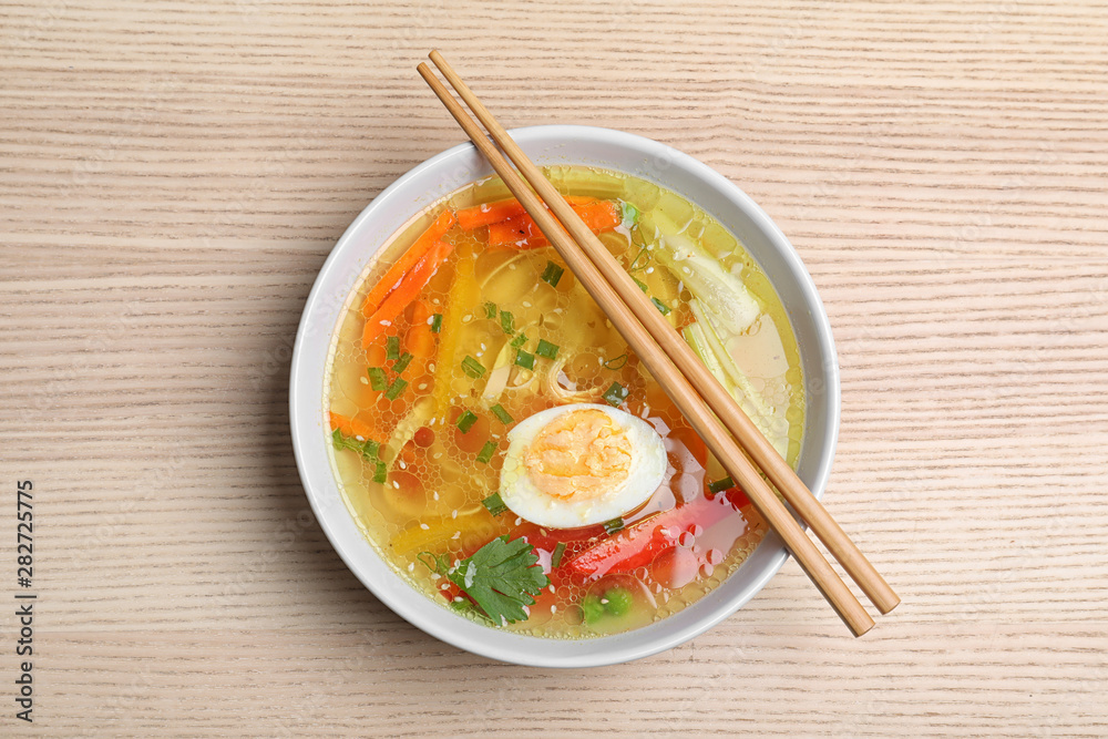 Bowl of tasty ramen with noodles, vegetables and chopsticks on wooden table, top view Bowl of tasty ramen with noodles, vegetables and chopsticks on wooden table, top view