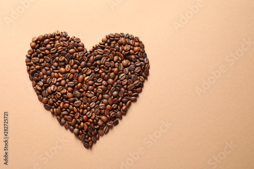 Heart shaped pile of coffee beans on light orange background, top view with space for text