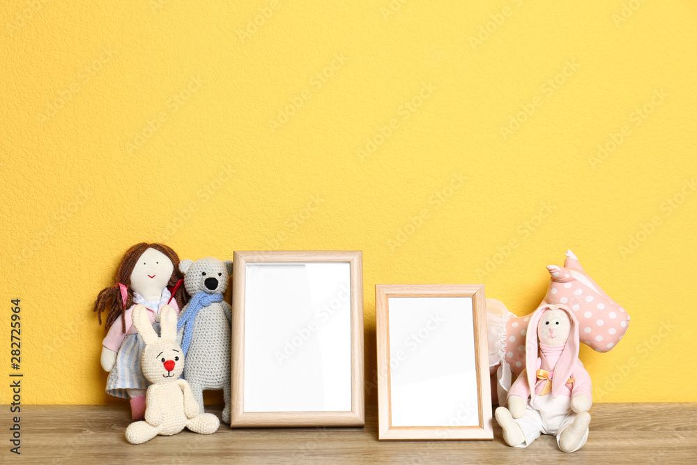 Soft toys and photo frames on table against yellow background, space for text. Child room interior