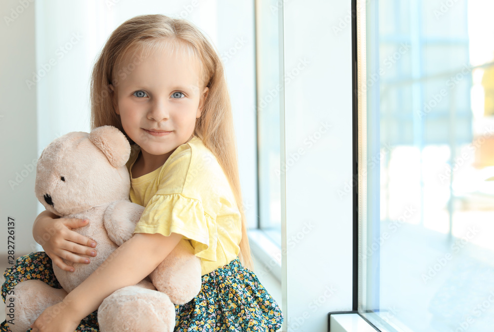 Pretty little girl with teddy bear near window in room Pretty little girl with teddy bear near window in room