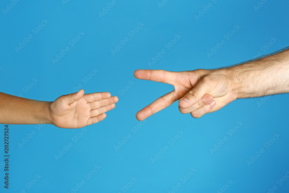 Little child and his father playing rock, paper and scissors on blue background, closeup