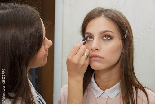 Makeup artist creates eyeliner on the face of the model.