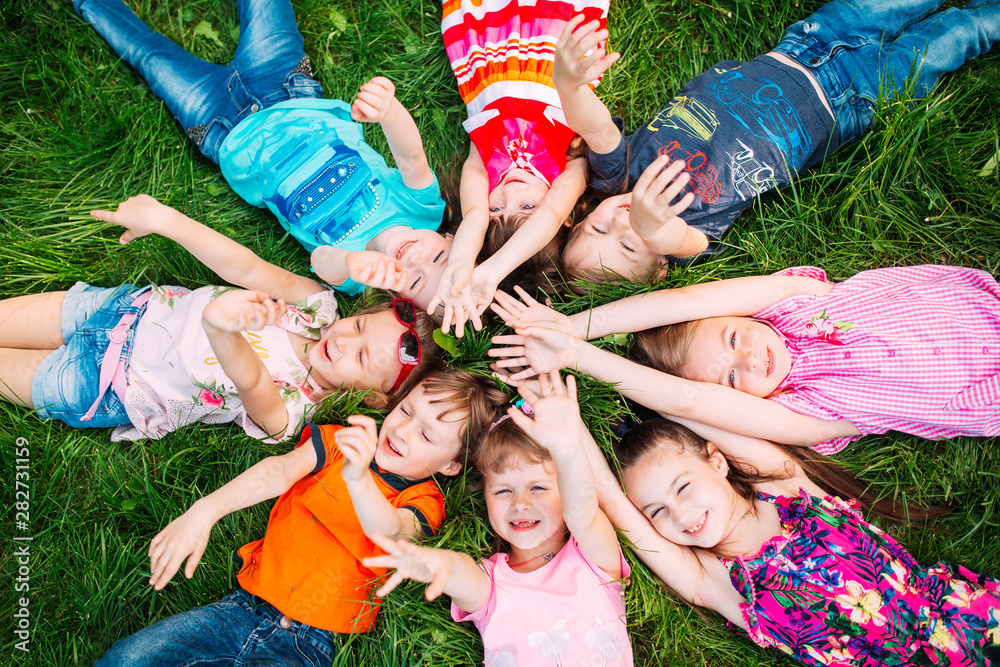Fototapeta premium A group of children lying on the green grass in the Park. The interaction of the children.