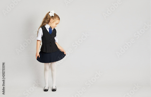 The little girl tried on a school uniform for the first time. A girl in a school uniform looks at herself from the side. Little girl in uniform on a white background.