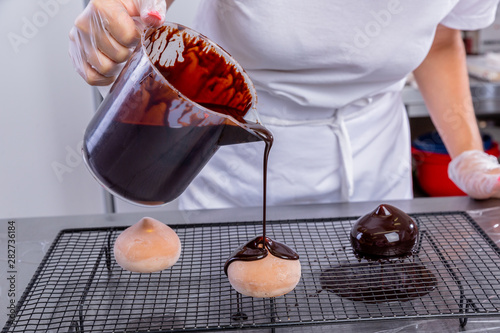 The pastry chef in the kitchen glazes pastries. Cook pours chocolate icing from a bowl onto cakes. Master class in the kitchen. The process of cooking. Step by step. Tutorial. Close-up