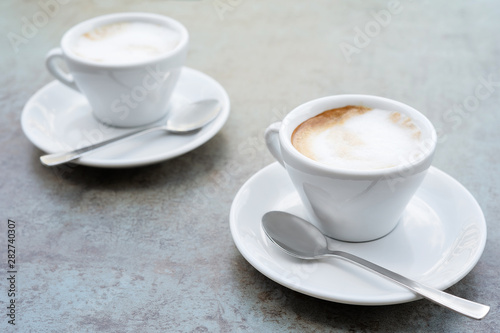 Two cups of cappuccino on a textured grey background. Street cafe. Close-up.