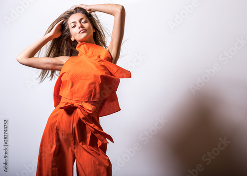 Young model woman in orange dress pose in studio.