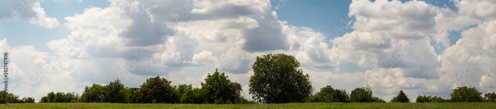 Fields and forests of Bulgaria before the rain. Cumuliform cloudscape on blue sky. The terrain in southern Europe. Fantastic skies on the planet earth. The sun is hidden. Panorama.