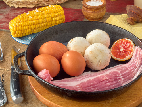Eco chicken eggs.Champignons.Bacon of pork belly are fried in a black cast iron skillet.On wooden background 