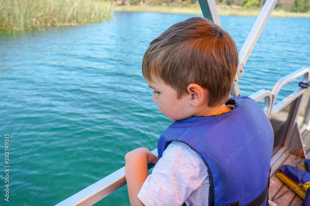 Cute little boy enjoying ride on a small boat. Little kid in the bow of a boat with his blue life jacket having fun. Travel adventure family vacation.