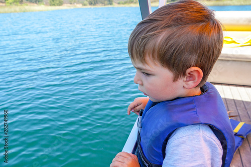 Cute little boy enjoying ride on a small boat. Little kid in the bow of a boat with his blue life jacket having fun. Travel adventure family vacation. photo