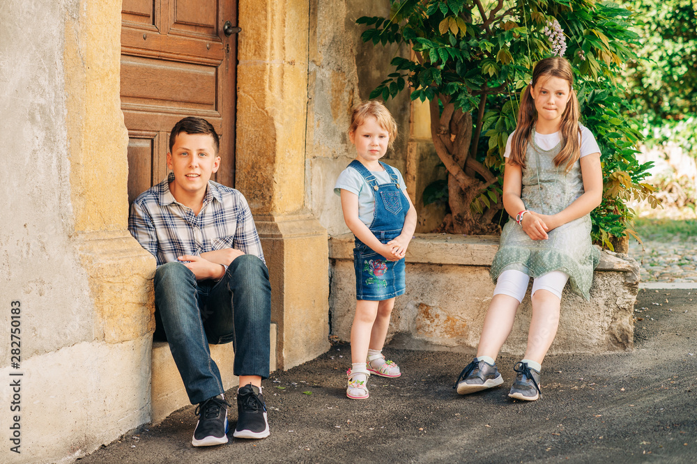 Fototapeta premium Portrait of three funny kids posing outdoor, teenage boy with little sisters, happy family