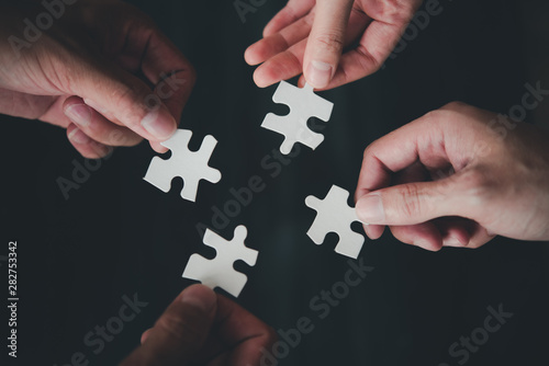 Teamwork concept using white puzzle pieces being fitted together by three male and female hands in a challenge, brainstorming and solution concept.