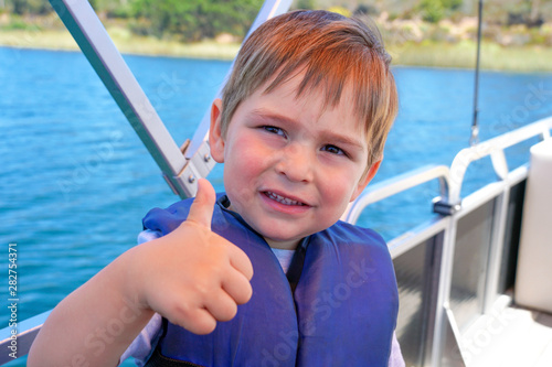 Cute little boy enjoying ride on a small boat. Little kid in the bow of a boat with his blue life jacket having fun. Travel adventure family vacation. photo