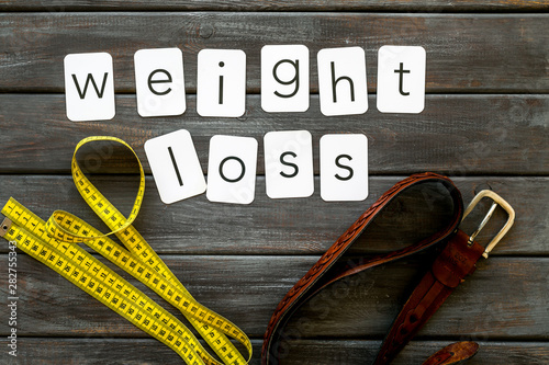 weight loss text with belt and measuring tape on wooden background top view