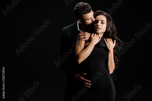 handsome man kissing beautiful girl with closed eyes isolated on black