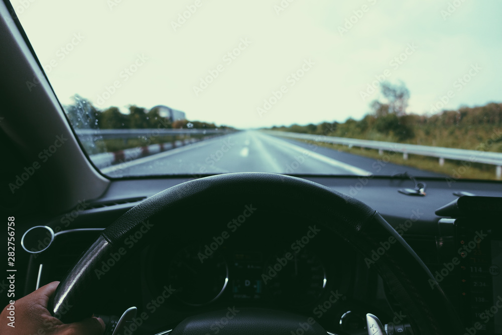 Inside view, hand of a driver on steering wheel of a car with empty asphalt road background. High-quality free stock image of driver hands on the steering wheel inside. Summer trip or vacation by car