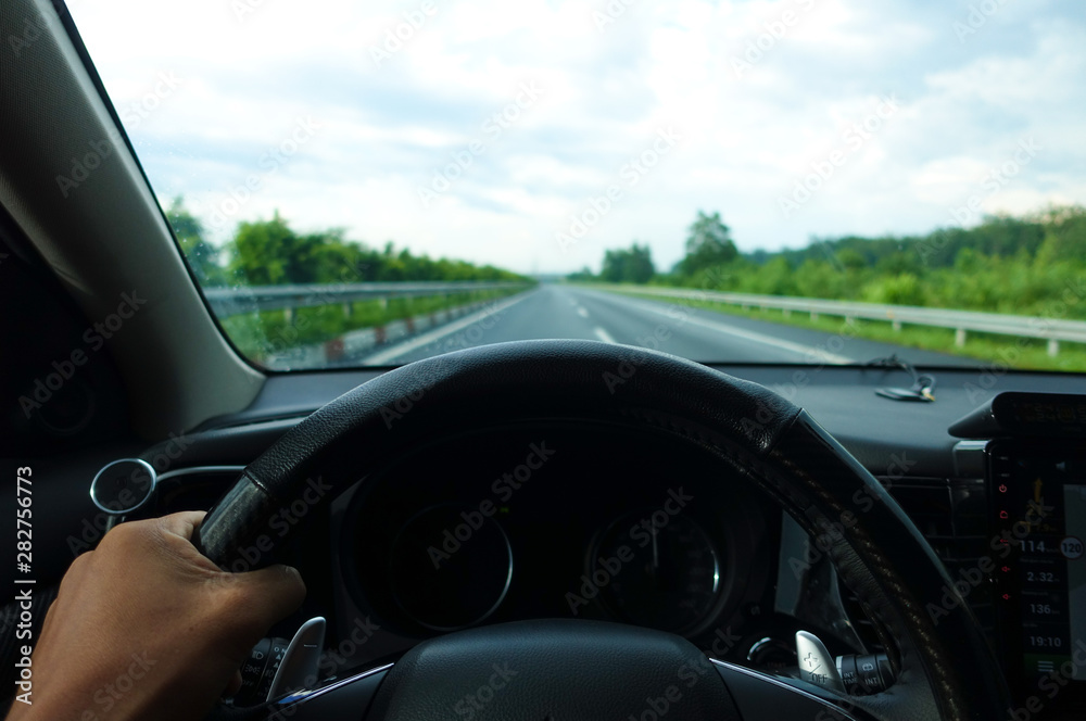 Inside view, hand of a driver on steering wheel of a car with empty asphalt road background. High-quality free stock image of driver hands on the steering wheel inside. Summer trip or vacation by car