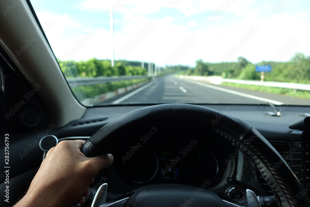 Inside view, hand of a driver on steering wheel of a car with empty asphalt road background. High-quality free stock image of driver hands on the steering wheel inside. Summer trip or vacation by car