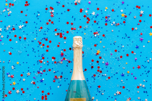 Champagne bottle with colorful party streamers for celebration on blue background top view pattern