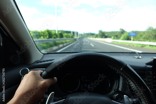 Inside view, hand of a driver on steering wheel of a car with empty asphalt road background. High-quality free stock image of driver hands on the steering wheel inside. Summer trip or vacation by car © jangnhut