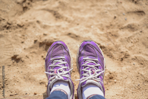 Happy woman resting on the beach. Women's feet in sneakers on the sand background. Vacation.