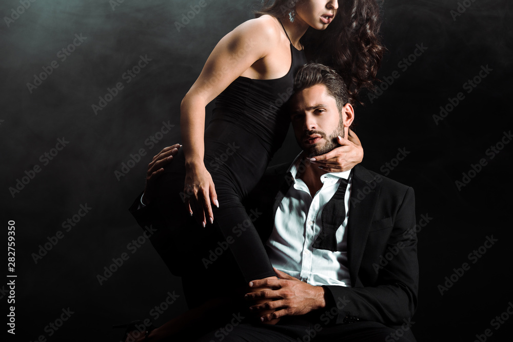 cropped view of woman standing and embracing bearded man in suit on black with smoke cropped view of woman standing and embracing bearded man in suit on black with smoke