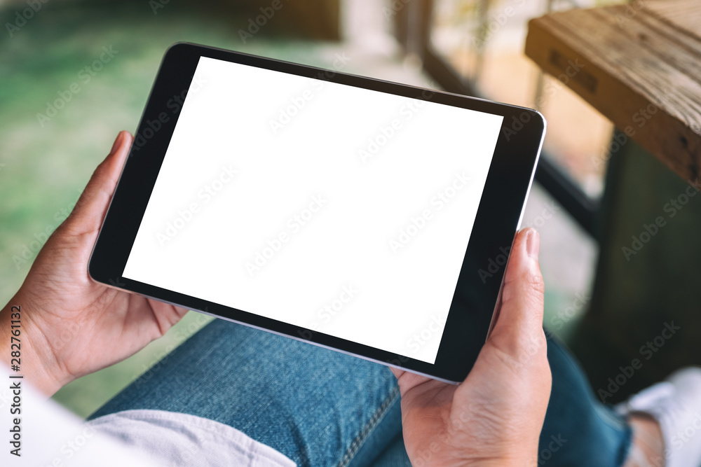 Mockup image of a woman sitting and holding black tablet pc with blank white desktop screen