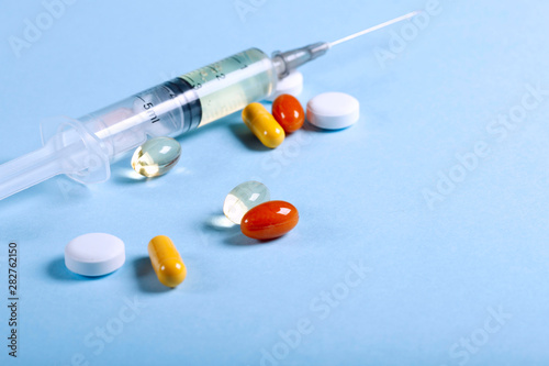 A lot of bright colored medicine pills and syringe on a blue background. Cropped shot, horizontal, close-up, free space. Medicine concept. Crisis of opioid painkillers and addiction concept.