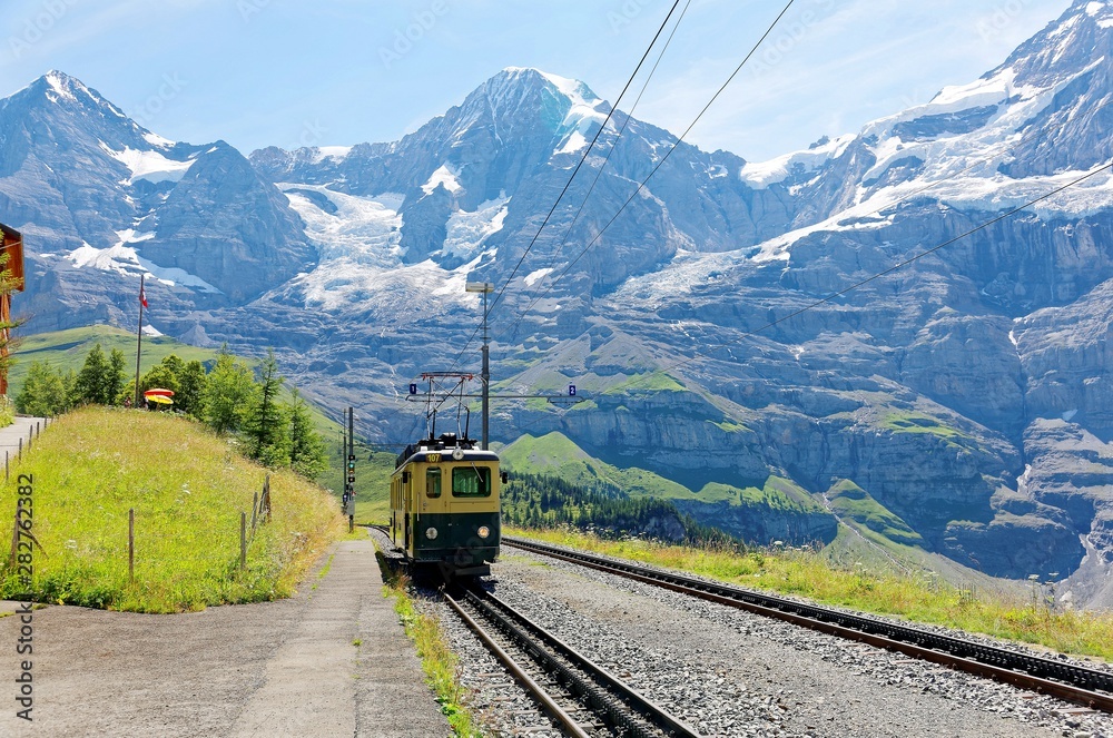 A cog wheel train traveling on the mountain Railway from Wengen to Kleine Scheidegg station with majestic Swiss Alps ( Eiger, Monch, Jungfrau ) in background, in Bernese Highlands, Switzerland, Europe