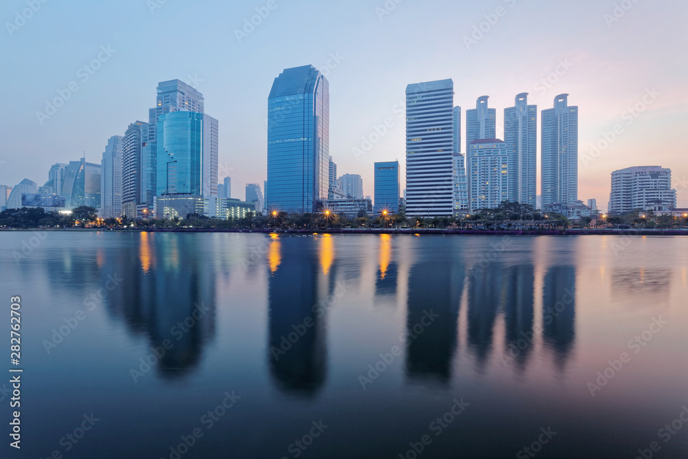 Beautiful city skyline of Bangkok at dawn with lakeside skyscrapers and reflections ~ Morning view of glass curtain walled buildings reflected on smooth lake water in Benjakiti Park, Bangkok Thailand