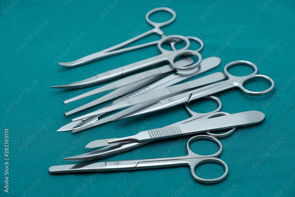Basic surgical instrument forceps tweezers scissors in emesis or plus basin and scalpel on surgical green drape fabric Basic surgical instrument forceps tweezers scissors in emesis or plus basin and scalpel on surgical green drape fabric