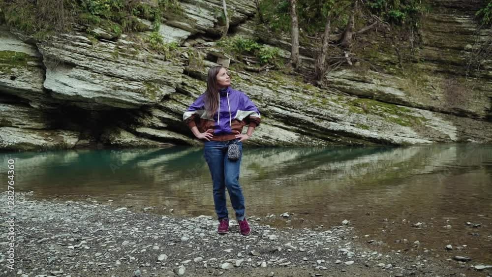 Beautiful girl stands puting her hands on the hips on the bank of a clean river Beautiful girl stands puting her hands on the hips on the bank of a clean river