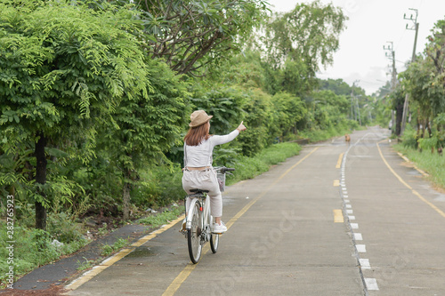 Pretty girl with straw hat is happy riding with bike down wide beautiful park alley with trees around on sunny summer day. © blindturtle