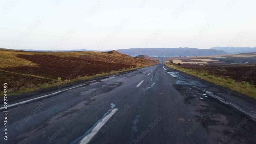 View from inside car on empty hilly road leading to horizon line at sunset or sunrise View from inside car on empty hilly road leading to horizon line at sunset or sunrise