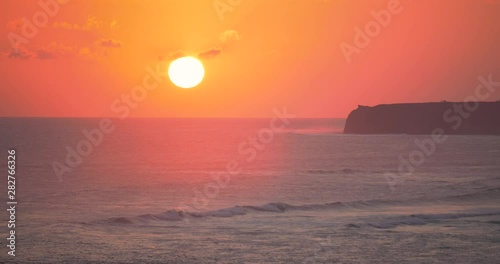 Calm and relaxing view of golden sun setting below horizon and slow moving waves, Indonesia
