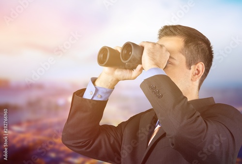 Young handsome business man in black suit using binoculars