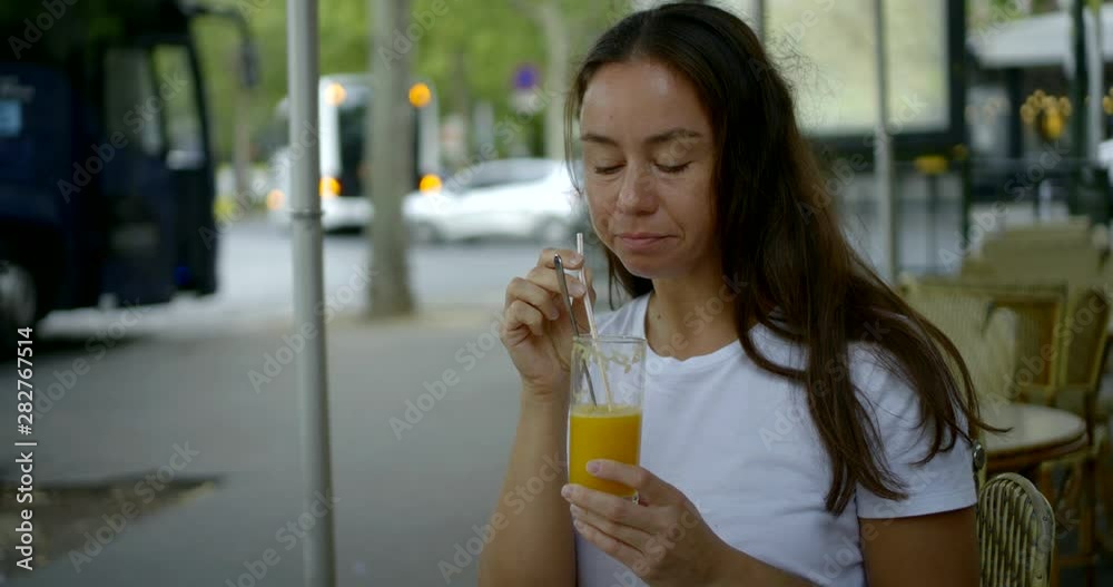Close-up portrait of a dark-haired middle-aged woman who sits on the street in a cafe. She drinks orange juice from a transparent large glass from a tube. Close-up portrait of a dark-haired middle-aged woman who sits on the street in a cafe. She drinks orange juice from a transparent large glass from a tube.