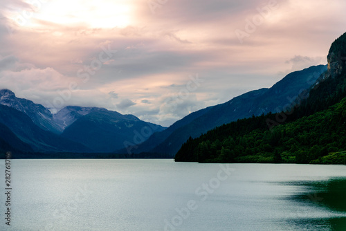 Mountains surround a shimmering lake illuminated by a cloud covered sky