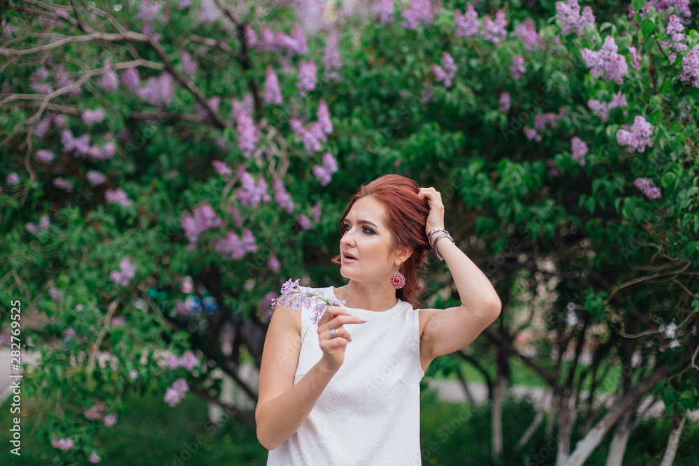 Charming woman wearing beautiful white dress standing next to lilac bush. Copy space. Charming woman wearing beautiful white dress standing next to lilac bush. Copy space.