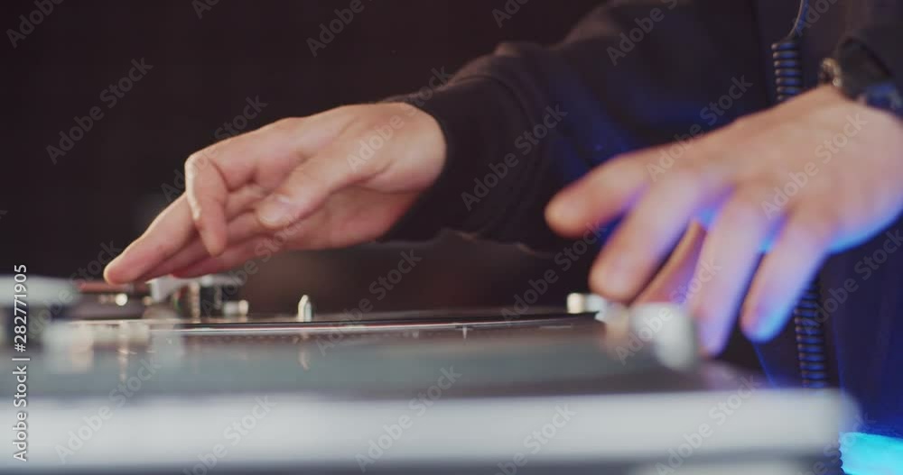 Closeup Dj turning knobs and levers, scratching vinyl record making new sound. Front view creative music producer playing nice music tracks by mixing records on console. Recording studio interior.